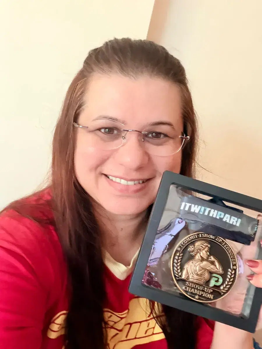 Priyanka smiling, holding her Show-Up Champion medal in its presentation frame.