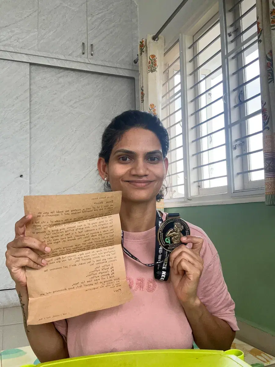 Richa smiling, holding up the typed letter from Pari in one hand and her Show-Up Champion medal on its lanyard in the other.