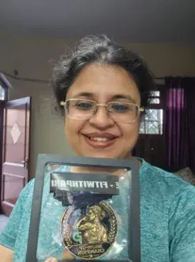 Shubhda smiling, holding her Show-Up Champion medal in its presentation frame.