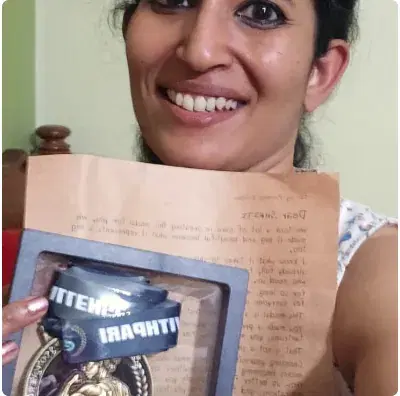 Smriti smiling behind the handwritten letter from Pari, her framed Show-Up Champion medal held in front of it.
