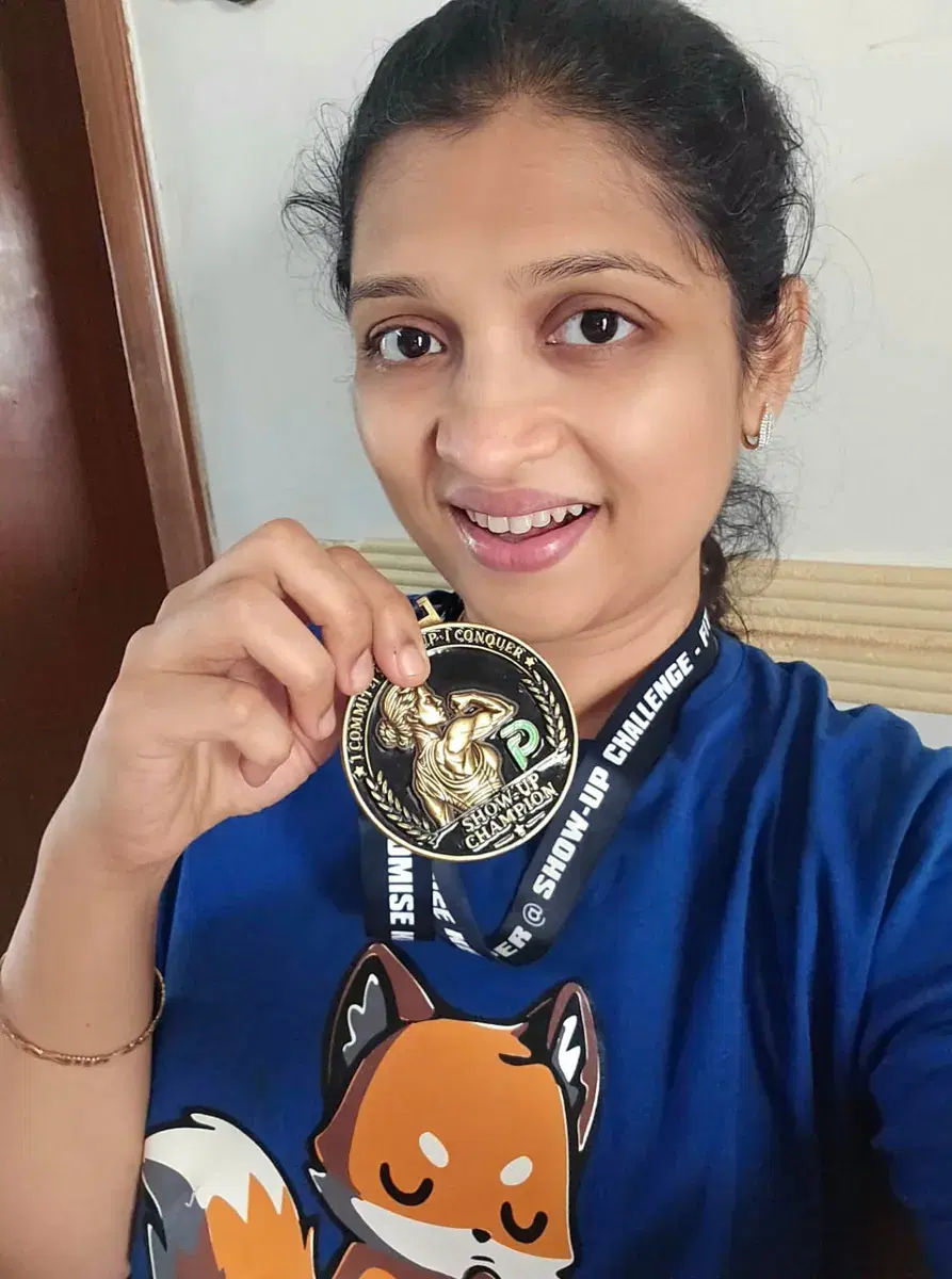 Swarna wearing her Show-Up Champion medal on its lanyard and holding it up to the camera.
