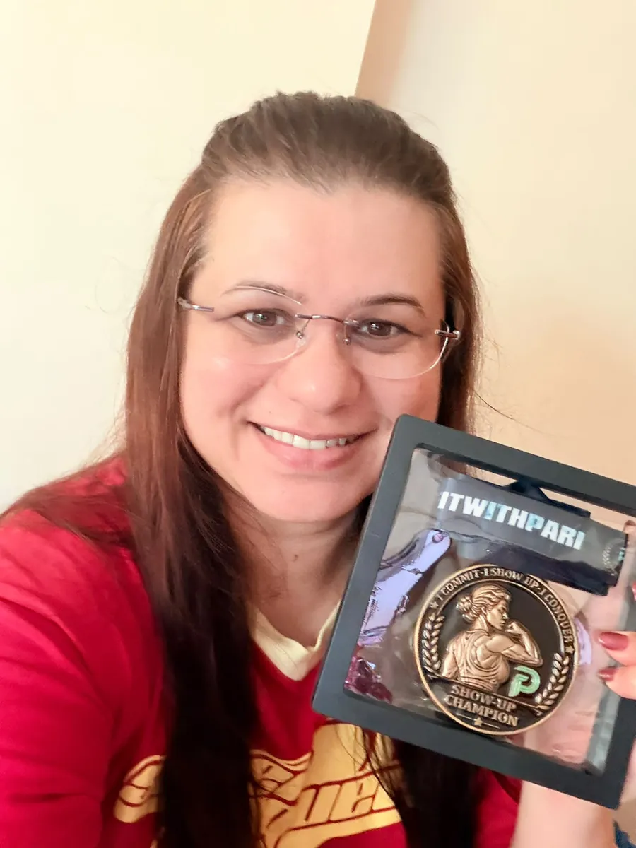 Priyanka smiling, holding her Show-Up Champion medal in its presentation frame.
