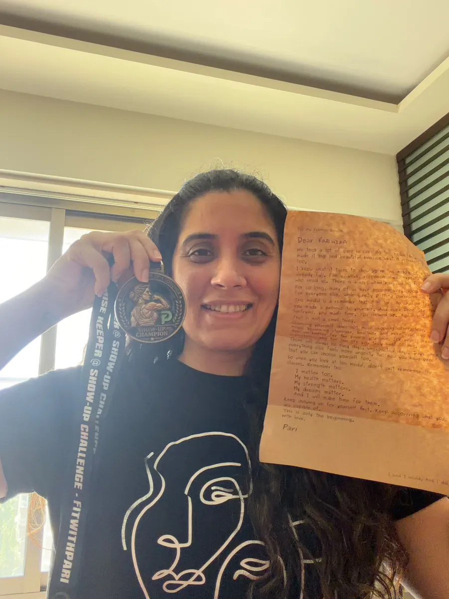 Radhika holding up her Show-Up Champion medal and the handwritten letter from Pari.