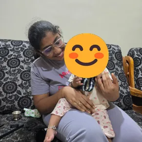 Sandhya smiling at home on her sofa, the lanyard of her Show-Up Champion medal in view.