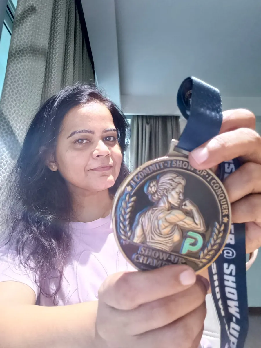 Shweta holding her Show-Up Champion medal, the engraving facing the camera.