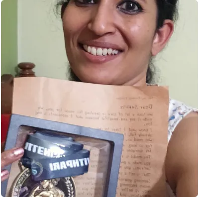 Smriti smiling behind the handwritten letter from Pari, her framed Show-Up Champion medal held in front of it.